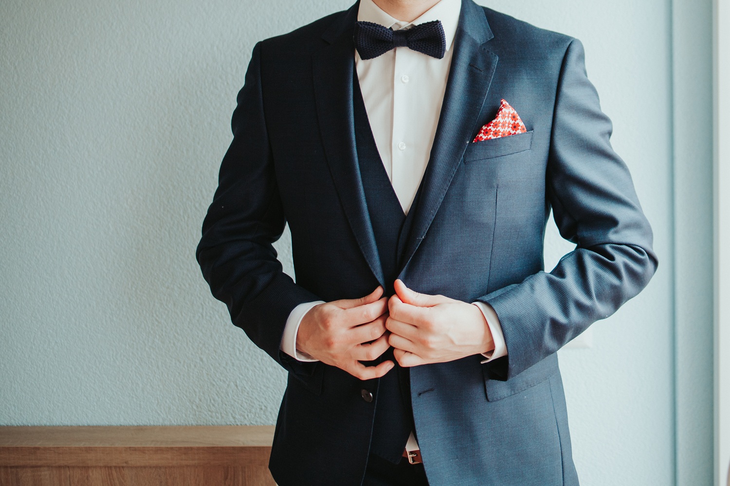 Man dressed in a fine suit with bowtie buttoning his jacket